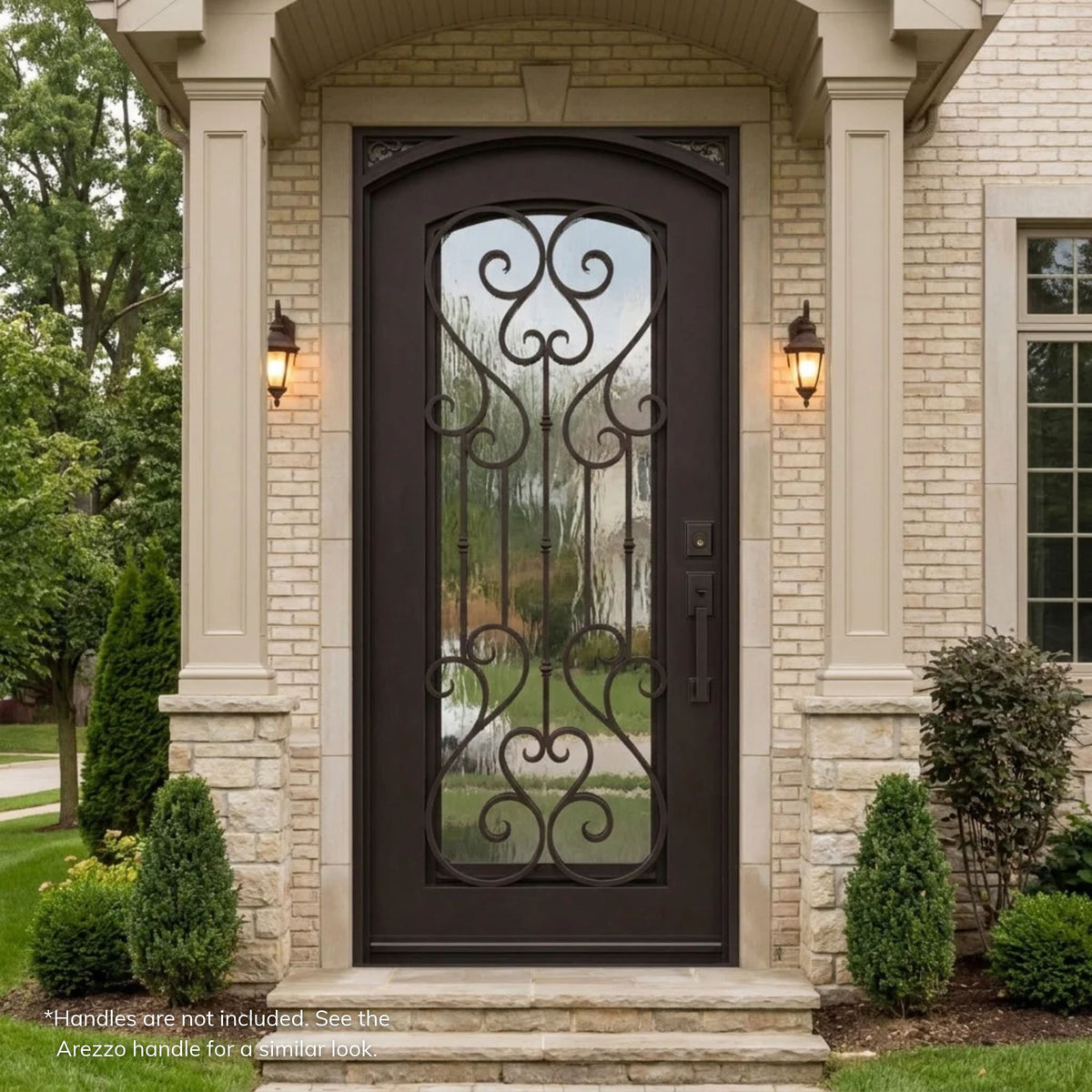 Anastasia dark bronze wrought iron single entry door with an arched top and full-length scrollwork over Flemish glass, set between columns on a light brick traditional home