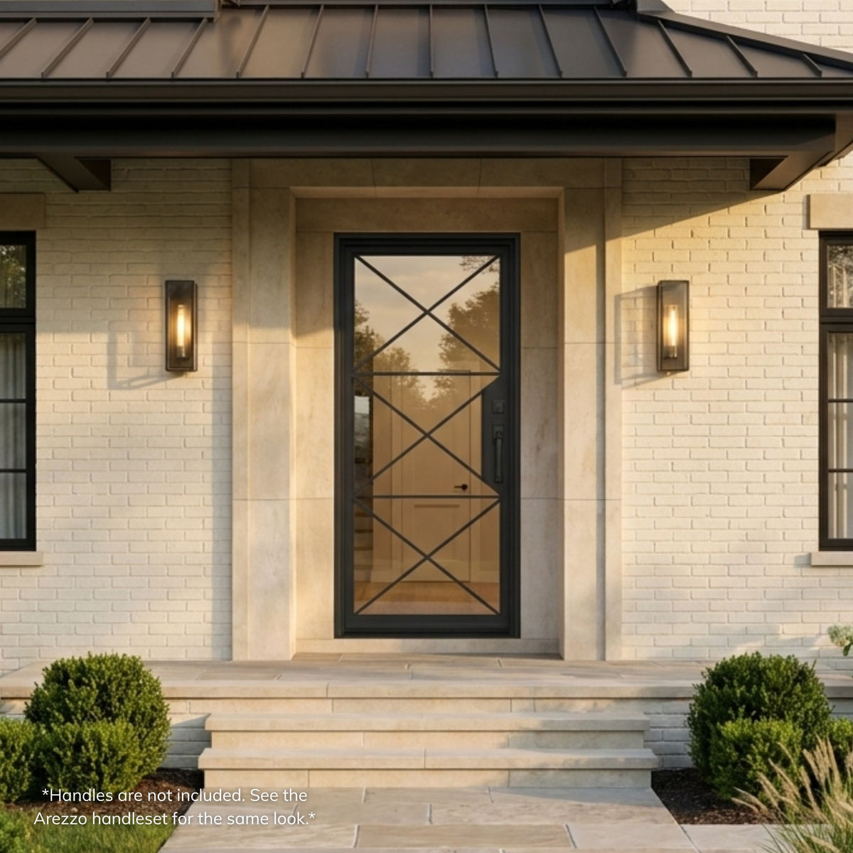 Bella wrought iron single entry door, matte black finish with clear glass and X-pattern iron overlay, installed on a white brick modern farmhouse exterior with lantern sconces
