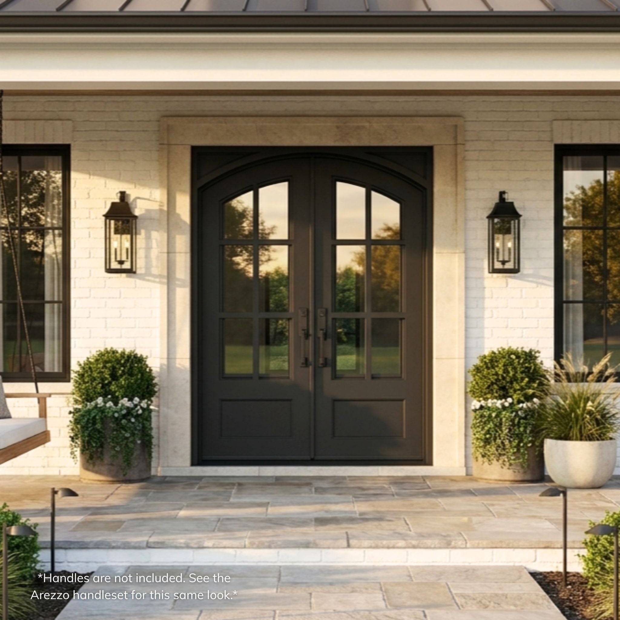 Elizabeth double iron entry door, matte black finish with arched divided-lite glass panels, installed on a white brick farmhouse exterior with covered porch, installed view
