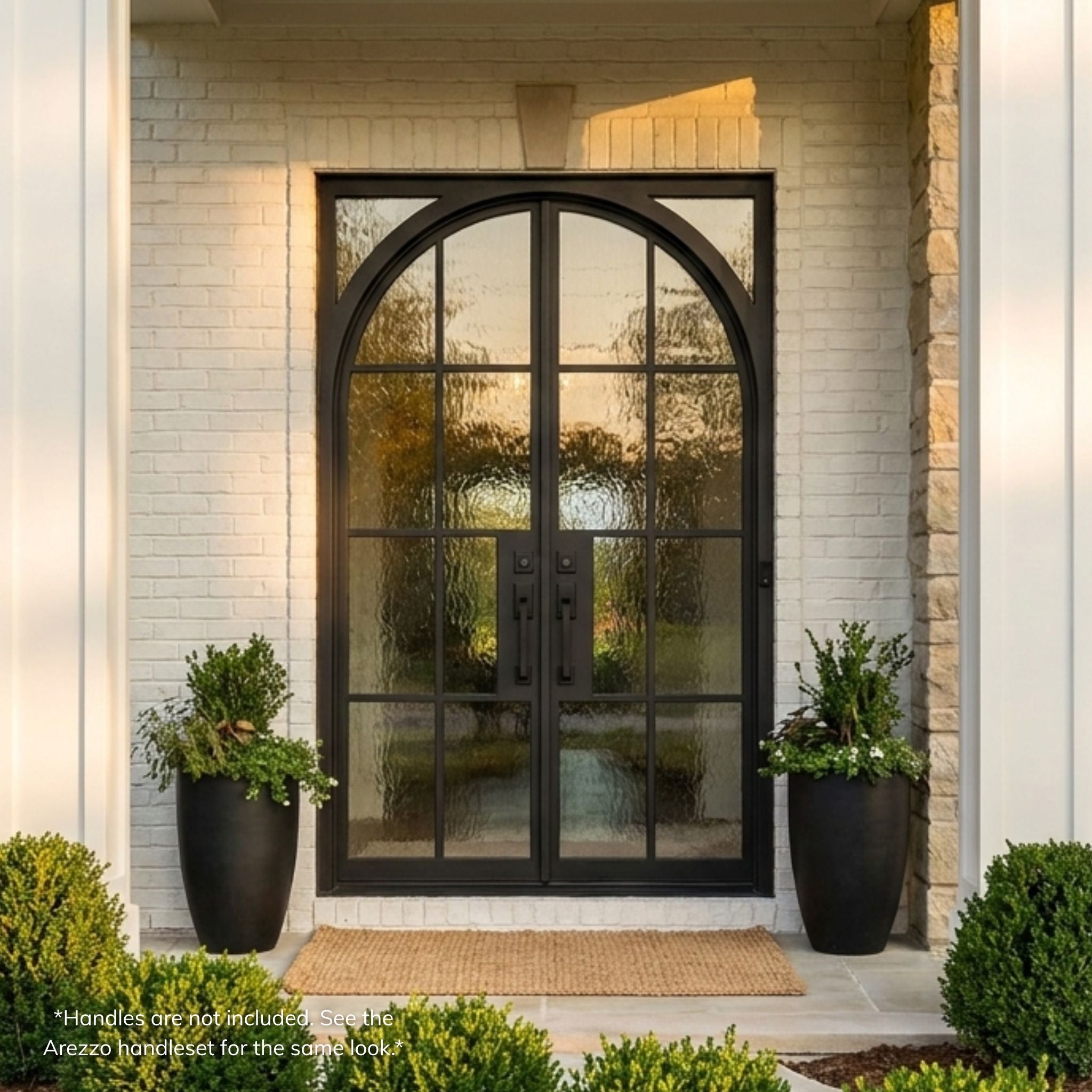 Geoffrey wrought iron double entry door, matte black finish with full-view divided-lite glass and Flemish textured glass, square-top with arch-top leaf design, installed on a white brick home exterior