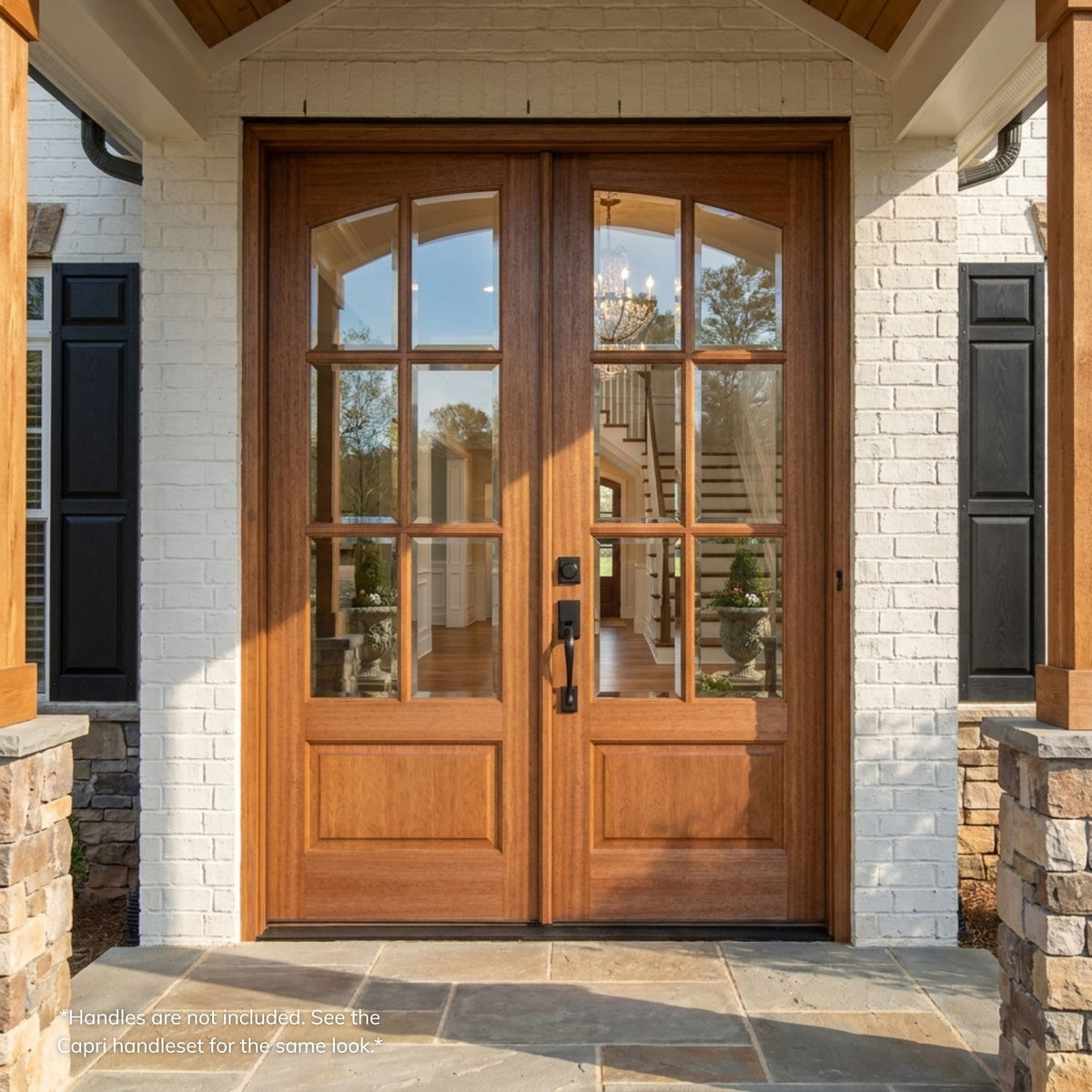 Mahogany double entry door in a natural wood finish, featuring a 6-lite arch clear glass on each leaf over a raised panel lower section, installed on a white brick home with black shutters.